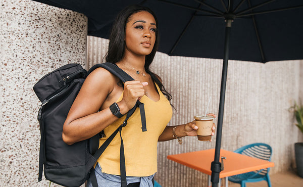 Woman wearing the Shadow Guide 33 over one shoulder and holding an iced coffee drink.